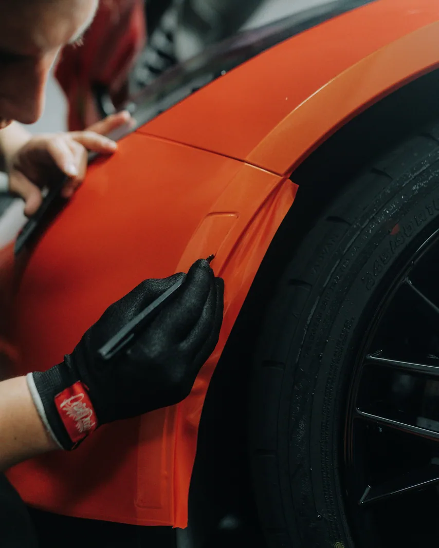 Worker applying material to a car body in a workshop.