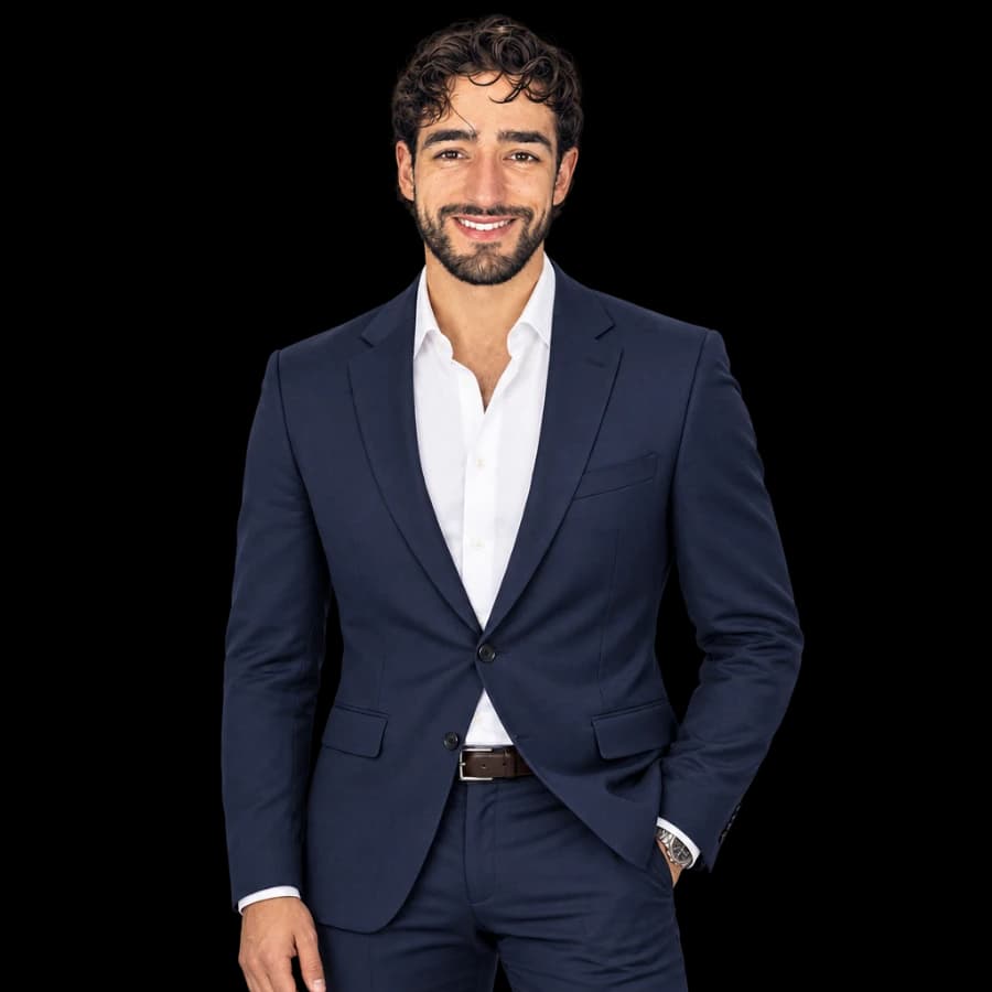 Ángel Álvarez standing and smiling, with curly hair, a beard, a navy blazer and a white shirt.
