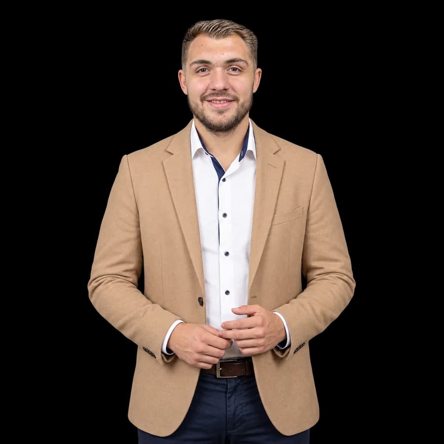 Víctor M. Gallego, de pie y sonriendo, con pelo castaño claro peinado hacia atrás, barba, americana color camel y camisa blanca de cuello azul marino.